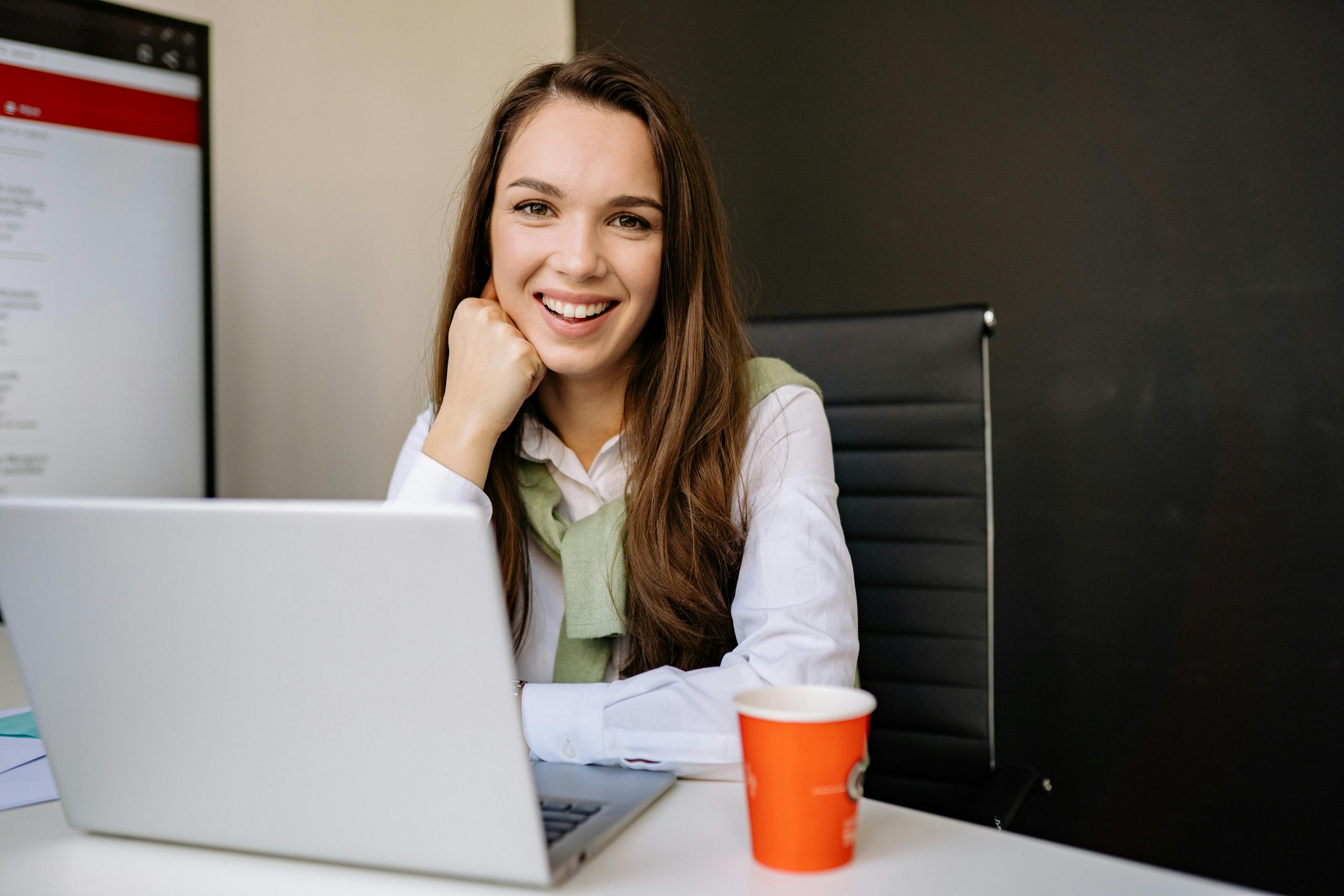 smiling woman sitting at a desk with a laptop and a cup of coffee