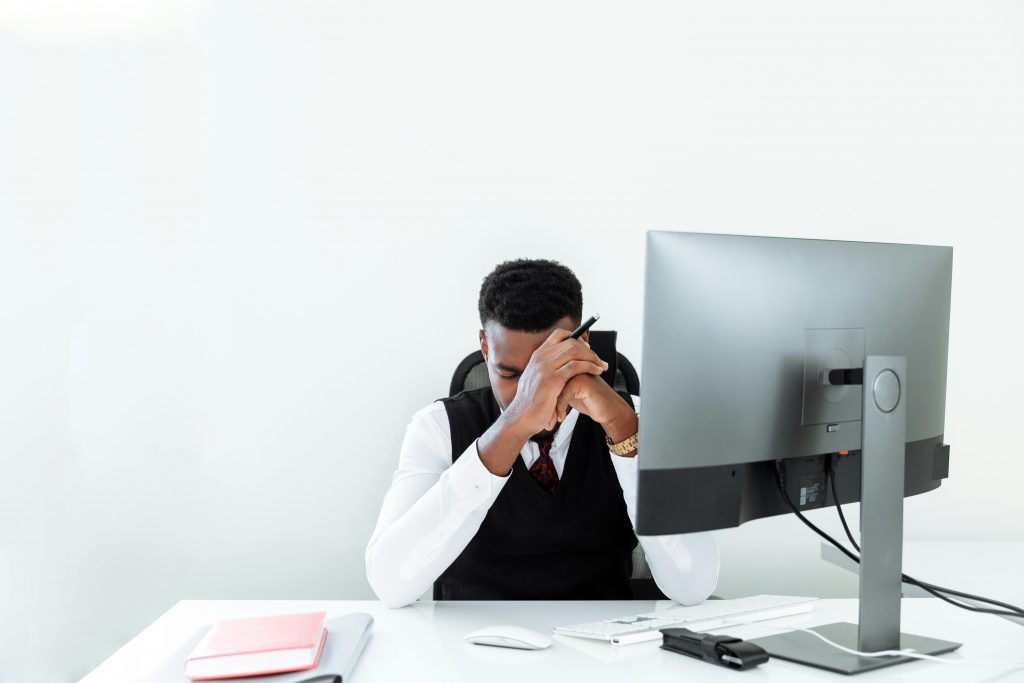 stressed man in business attire resting his head on his hands at a desk with a computer