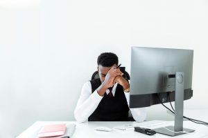 stressed man in business attire resting his head on his hands at a desk with a computer